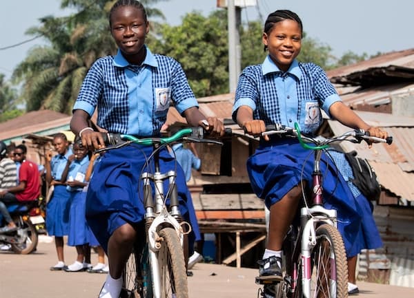 Two students in school uniforms riding bicycles to school